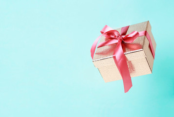 Gold color gift box with pink ribbon on blue background close-up, copy space. Levitation