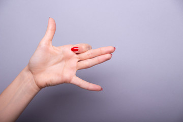 Beautiful women 's hands with red manicure show gesture against grey background.