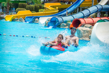 In the summer, on a bright sunny day, in a water park, father and daughter slide down the hill.