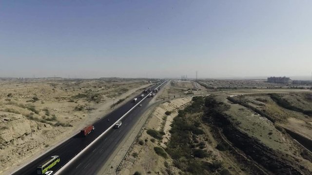 An aerial slow mo view of a highway and city, The heavy trawlers and cars are moving on the highway, an interchange is connecting.