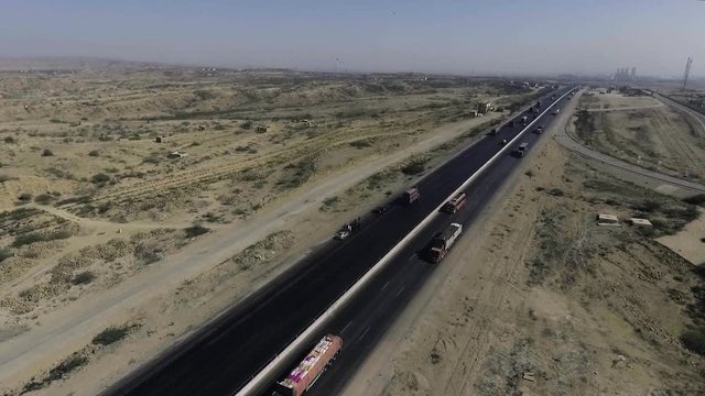 An aerial slow mo view of a highway and city, The heavy trawlers and cars are moving on the highway, an interchange is connecting.