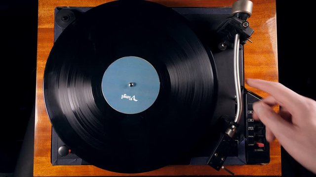 Person turns on a musical player, placing a needle on a vinyl record.