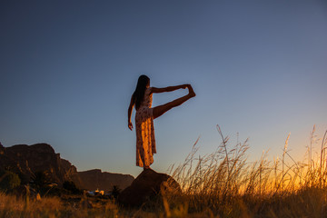 Silhouette of a beautiful woman balancing on a rock at sunset or sunrise.