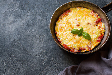 Omelet, scrambled eggs with tomatoes and cheese in a pan on a dark table.