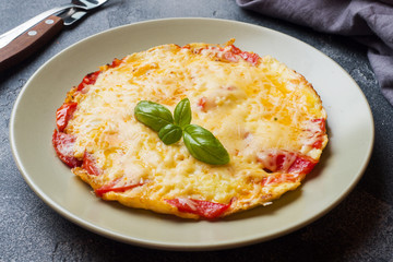 Omelet, scrambled eggs with tomatoes and cheese in a plate on a dark table.
