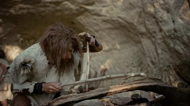 Primeval Caveman Wearing Animal Skin Trying to make Fire with Bow Drill Method. Neanderthal Kindle First Man-Made fire in the Human Civilization History. Making Fire for Cooking. Slow Motion Arc Shot