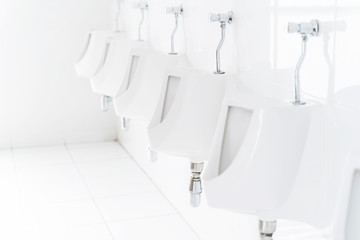 Closeup of urinals row in public restroom, clean white color tone.