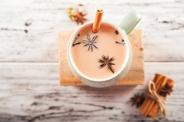 Details of still life in the home interior living room. Beautiful Cup of tea with milk, star anise, cinnamon on a wooden background. Cozy autumn-winter concept. Masala is a traditional hot spicy drink