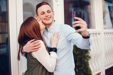 handsome young guy in a blue shirt standing in a sunny summer city along with her cute girl in a white shirt and they use the phone