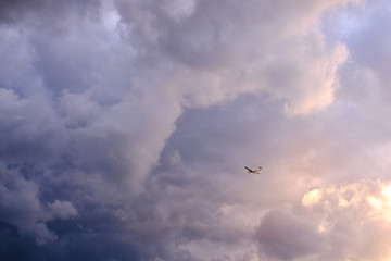 Fototapeta premium Tiny plane in front of a colorful and cloudy sky in vivid evening athmosphere