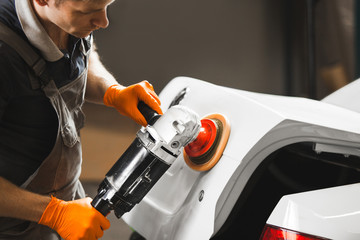 Worker polished white car with orbital polisher in auto repair shop, close-up. Vehicle detailing.