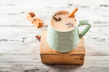 Details of still life in the home interior living room. Beautiful Cup of tea with milk, star anise, cinnamon on a wooden background. Cozy autumn-winter concept. Masala is a traditional hot spicy drink