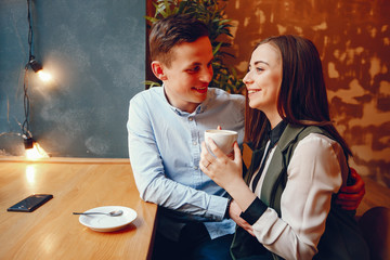 handsome young guy in a blue shirt sitting in a cafe along with her cute girl in a white shirt and they drinking a coffee