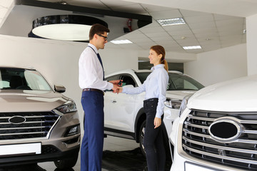 Car dealership sales person at work concept. Portrait of young sales representative wearing formal wear suit, showing vehicles at automobile exhibit center. Close up, copy space, background.