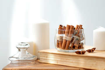 Fototapeta na wymiar Cinnamon sticks in glass jar, anise star, candles, vintage book on old rustic rustic wooden background. Cozy still life.