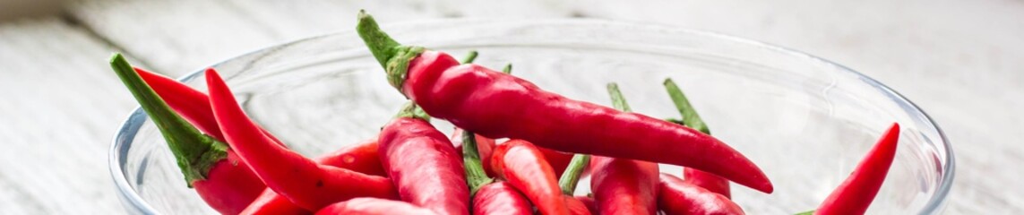 banner of Red chilli peppers in transparent bowl on white wooden background