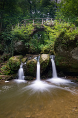 Fototapeta na wymiar idyllic small waterfall in lush green forest landscape with an old bridge above