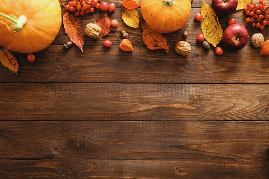 Autumn frame border made of pumpkins, dried fall leaves, apples, red berries, walnuts on wooden background. Thanksgiving, Halloween, Autumn Harvest concept. Flat lay composition, top view, copy space