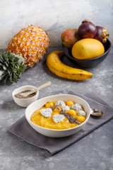 Smoothie bowl on gray background. Delicious mango smoothie topped with chia seeds, pieces of mango and dragon fruit. Healthy breakfast.