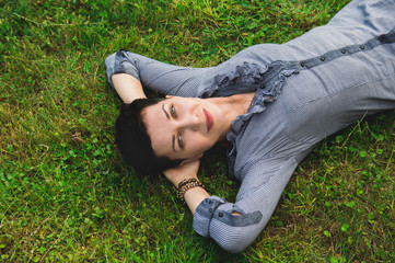 A young girl with dark short hair is lying on the green grass, with hands under her head.