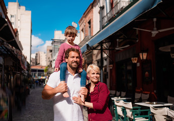 Young family with small daughter standing outdoors in town on holiday.