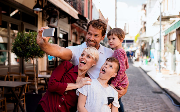 A young family with two small children standing outdoors in town, taking selfie.
