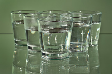 Alcoholic drink in clear glasses. Little cups isolated on green background. Frozen drinks on glass table.
