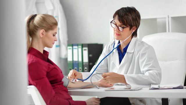 Positive female doctor checking pulse of woman patient using stethoscope medical equipment