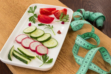 Vegetables in a ceramic plate on an uncouth board. Measuring tape. Low calorie diet concept.