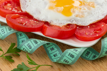 Sliced tomatoes and egg on a uncut board. Measuring tape. Low calorie diet concept
