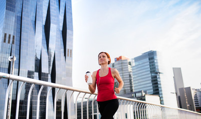 Young woman runner with earphones and water bottle jogging in city.