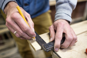 Carpenter using a straightedge to draw a line on a board marking a place for cutting.