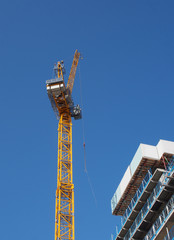 a view of a tall tower crane working on large construction sites against a blue sky