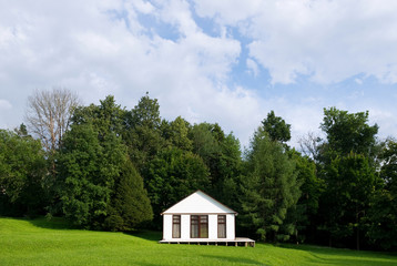 Fototapeta na wymiar a small white house with curtained windows stands in the center of a small slope against the background of the forest. front view