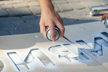 Hand holds an aerosol spray can, puts the image on the asphalt through a stencil
