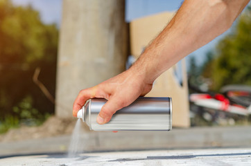 Male hand holds an aerosol spray can, draws graffiti on the asphalt
