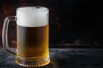 Mug of light beer with drops of water on a dark rusty background copy space