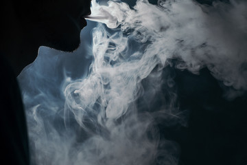 Closeup of a vaping man holding a mod. A cloud of vapor. Black background.