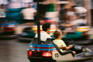 blurred image of father and son enjoying car bumper ride on funfair.
