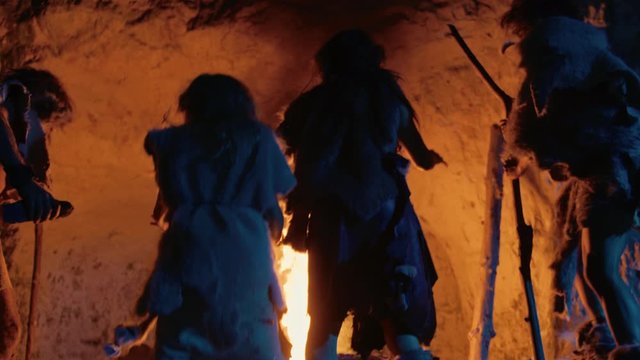 Tribe of Prehistoric Hunter-Gatherers Wearing Animal Skins Dance Around Bonfire Outside of Cave at Night. Neanderthal / Homo Sapiens Family Doing Pagan Religion Dancing Near Fire Back View Slow Motion