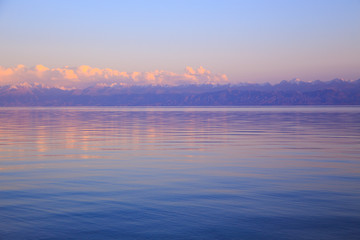 Beautiful sunset on a lake in the mountains. Kyrgyzstan, Issyk-Kul Lake. Bright sky, background in warm colors.