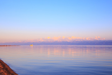 Beautiful sunset on a lake in the mountains. Kyrgyzstan, Issyk-Kul Lake. Bright sky, background in warm colors.