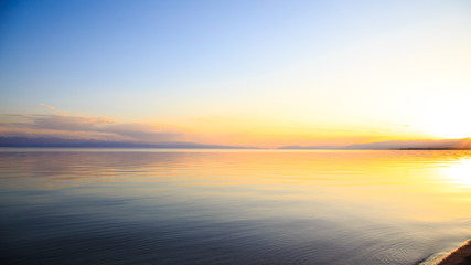 Beautiful sunset on a lake in the mountains. Kyrgyzstan, Issyk-Kul Lake. Bright sky, background in warm colors.