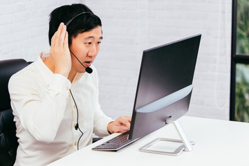 Young Asian male call center operator talking on headset phone. Customer support service...