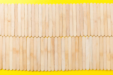 Many wooden ice cream sticks in row on yellow background, flat lay