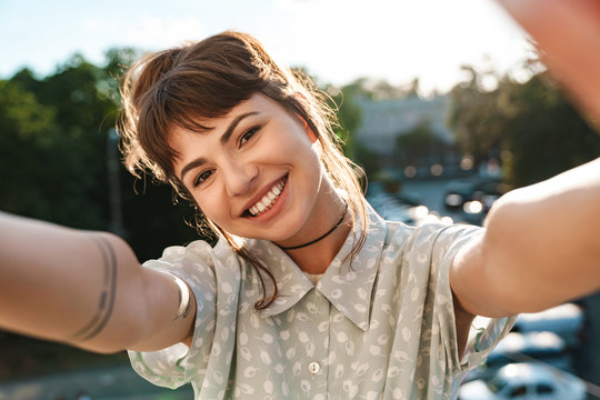 Happy emotional positive pretty woman on a balcony take a selfie by camera.