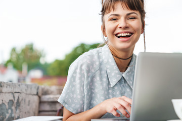 Emotional happy young beautiful woman using laptop computer on a balcony.