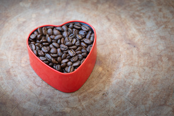 Coffee beans in a heart-shaped tin arranged on a wooden background.