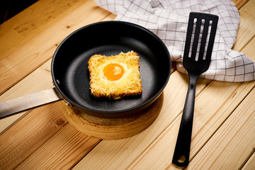Delicious toast with fried egg in pan on wooden kitchen table