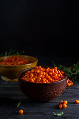 Berries and branches of sea buckthorn, bowls with berries on a dark wooden background
